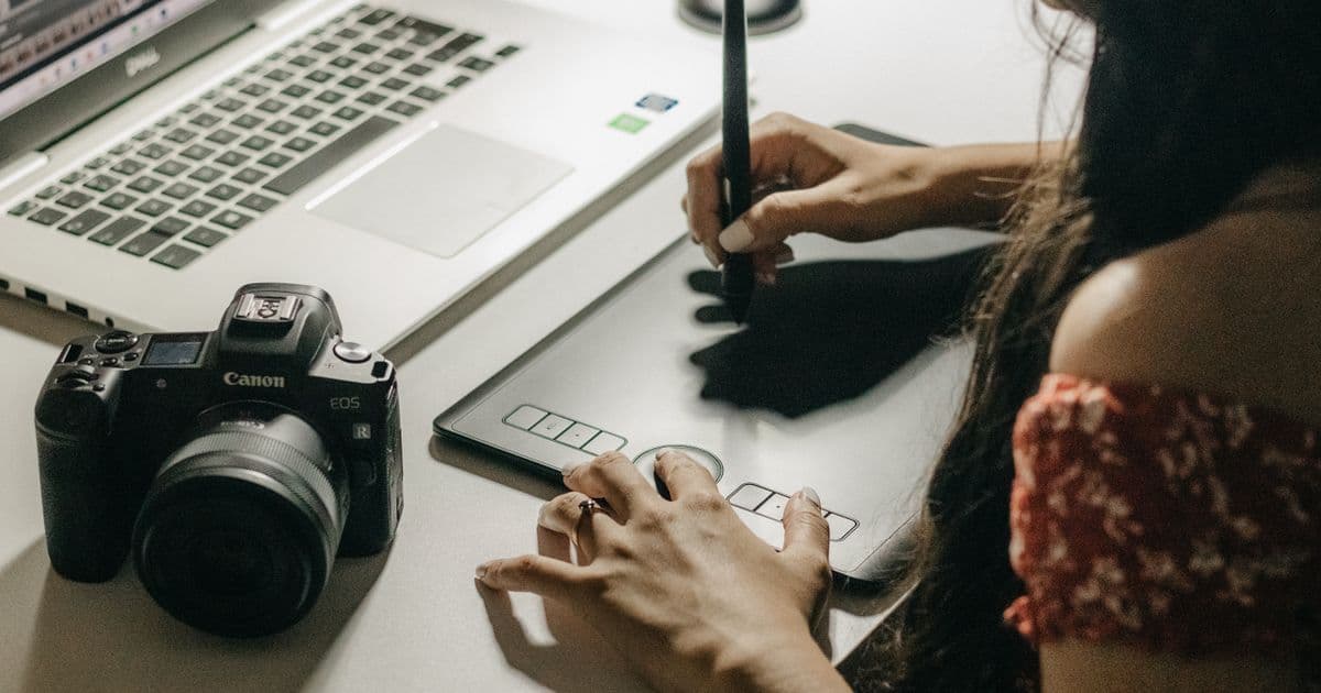 A designer drawing on a graphics tablet beside a laptop and camera