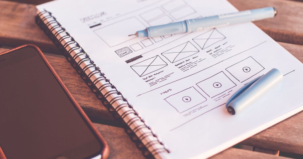 Hand-drawn app wireframes in a notebook, with a pen and a phone